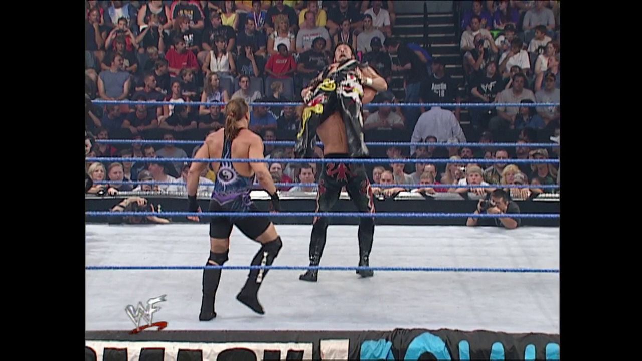 A frame from WWE SmackDown (July 26, 2001) at 52:46. Two wrestlers face off in a WWE SmackDown ring, with one performer elevated above the canvas mid-move. The packed crowd fills the arena stands while the blue-roped ring and WWF logo are visible in the foreground.