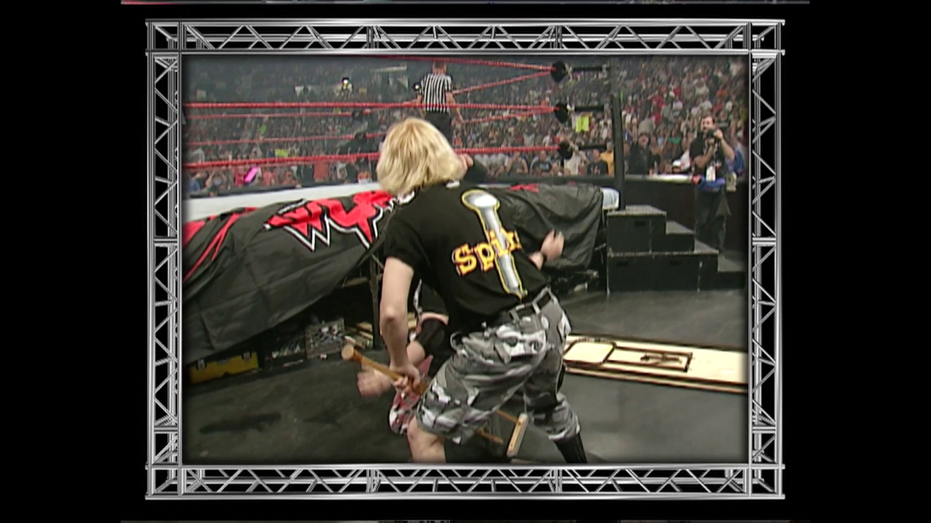 A frame from WWE Raw (July 9, 2001) at 19:40. A blonde wrestler in black and gold attire holds a microphone in a WWE Raw ring, facing the crowd. The arena is packed with spectators, and red ropes frame the wrestling ring with visible referee and audience in the background.