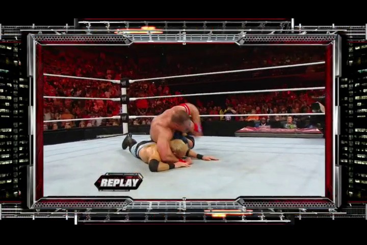 A frame from WWE Raw (June 20, 2011) at 2:14:39. A wrestler lies on the mat during a replay moment in a WWE Raw match, with the red-lit crowd visible in the background and the white ring ropes framing the action. The "REPLAY" graphic appears in the lower left corner of the broadcast frame.