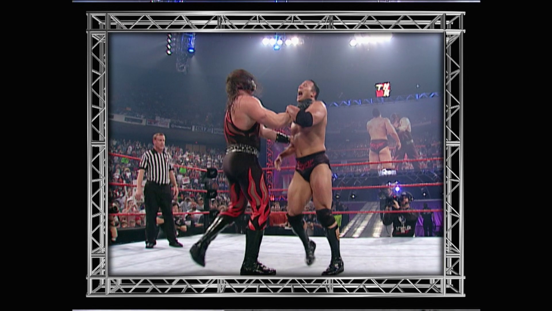 A frame from WWE Raw (January 1, 2001) at 1:24:07. Two wrestlers engage in combat in a WWE ring, with one in red and black attire grappling against his opponent. A referee in striped shirt stands nearby, while the arena crowd and overhead lighting are visible in the background.