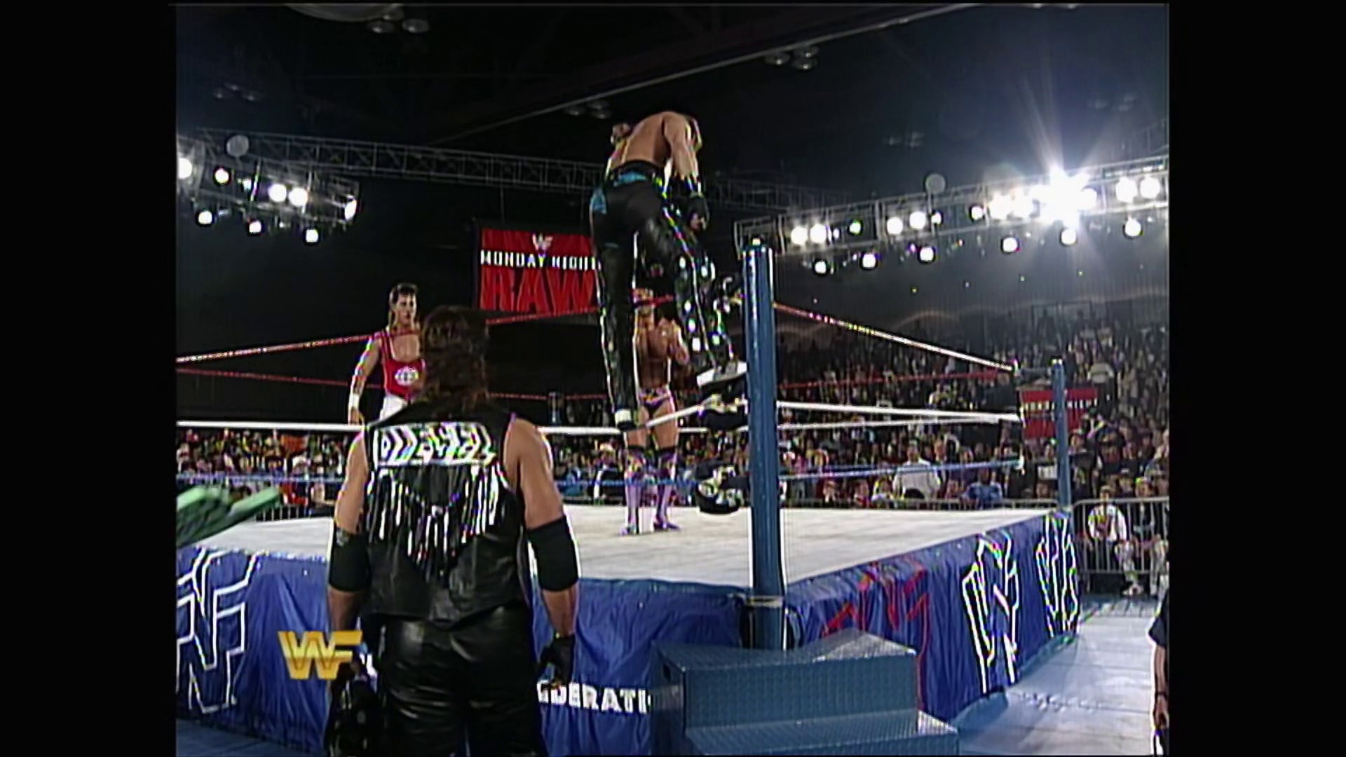 A frame from WWE Raw (February 21, 1994) at 21:26. A wrestler stands on the ring ropes during a WWE Raw match, with the crowd visible in the background under bright arena lights. The ring features WWF branding, and other wrestlers can be seen in the ring as the match unfolds.