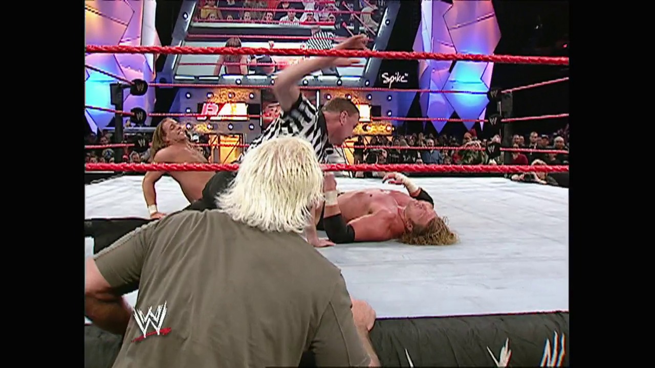 A frame from WWE Raw (December 29, 2003) at 1:26:09. A WWE Raw match in progress shows a wrestler with blonde hair in the ring, with another competitor on the mat. The red ropes, illuminated arena with purple lighting, and crowded audience are visible in the background, along with WWE graphics and the Spike branding.