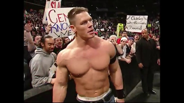 A frame from WWE SmackDown (February 25, 2005) at 1:24:54. A shirtless wrestler stands in a crowded arena surrounded by spectators holding signs during a WWE SmackDown event, with the audience visible in the background under arena lighting.