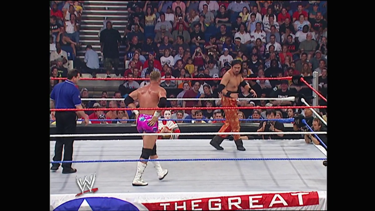 A frame from WWE Great American Bash (2004) at 1:11:28. A WWE wrestling match is underway in a packed arena, with two shirtless wrestlers in the red-roped ring. The crowd fills the stands in the background while "THE GREAT" text is visible at the bottom of the frame.