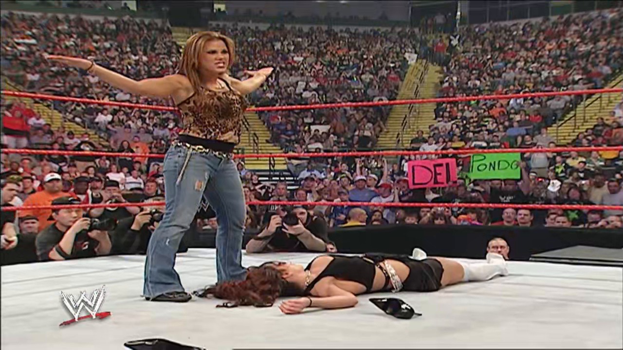 A frame from WWE Raw (April 2, 2007) at 1:03:09. A female wrestler stands victoriously with arms raised in the WWE ring while her opponent lies on the mat below. The packed arena crowd surrounds the red-roped ring, with the WWE logo visible in the corner.