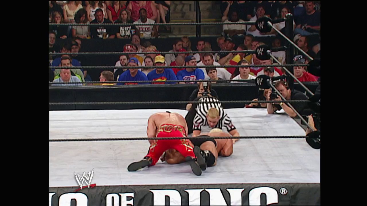 A frame from King of the Ring (2002) at 1:08:49. A wrestler in red and gold attire lies on the mat while a referee makes a count during a WWE match. The crowd fills the stands behind the ring as the "King of the Ring" event logo appears at the bottom of the screen.