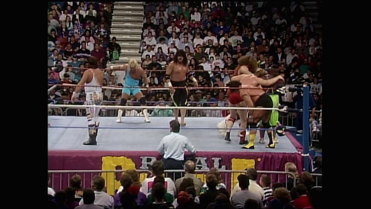 A frame from Royal Rumble (1993) at 1:52:41. # Royal Rumble 1993 - Wrestling Match Frame

A multi-wrestler match unfolds in a packed arena with wrestlers grappling in the ring while a referee in a light blue shirt oversees the action. The crowd fills the bleachers behind the burgundy-skirted ring, with visible signage and blue ring posts framing the wrestling spectacle.