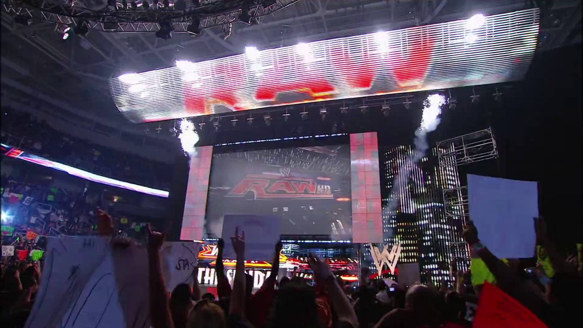 A frame from WWE Raw (March 22, 2010) at 0:55. # WWE Raw Arena Setup

A packed WWE arena during Raw with illuminated LED screens displaying the RAW HD logo, pyrotechnics bursting above the stage, and enthusiastic fans cheering in the foreground while the distinctive WWE ring and production set are visible in the center.