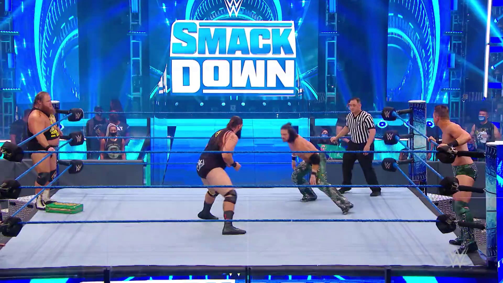 A frame from WWE SmackDown (August 7, 2020) at 1:13:03. # WWE SmackDown Visual Description

A multi-wrestler match unfolds in the WWE ring with the "SMACK DOWN" logo prominently displayed above. The brightly lit blue arena features wrestlers in action, a referee in striped shirt, and spectators visible in the background behind protective barriers.
