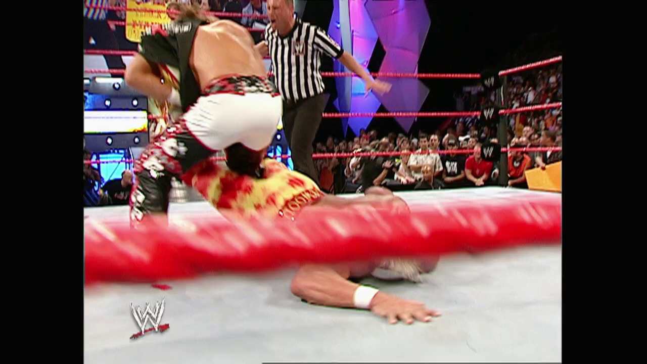 A frame from WWE Raw (August 15, 2005) at 1:32:18. A wrestler lies on the mat near the red rope while another competitor stands above in the ring during a WWE Raw match. A referee in a striped shirt oversees the action as the crowd watches from the stands in the background.
