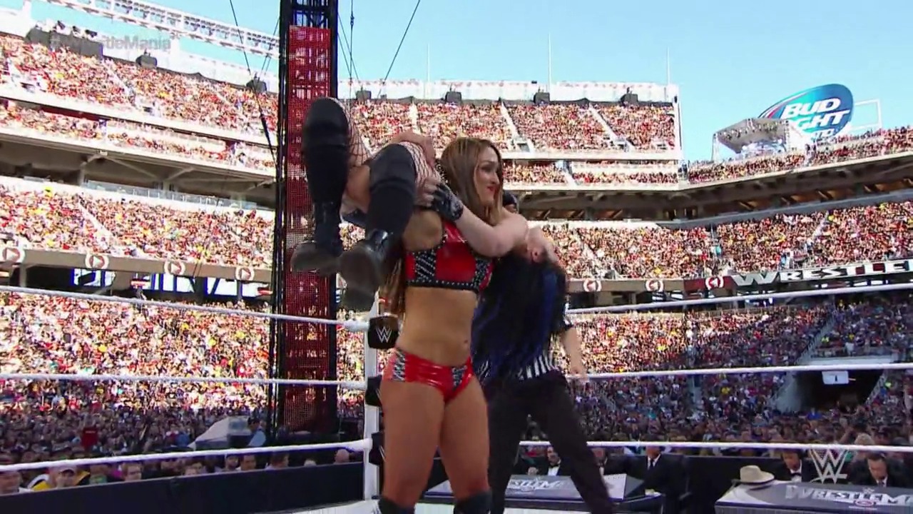 A frame from WrestleMania (2015) at 1:43:06. # WrestleMania 2015 - Ring Action

Two female wrestlers face off in the WWE ring during WrestleMania 2015, with one wearing red and black attire. The massive stadium is packed with thousands of cheering fans, and sponsorship logos including Bud Light are visible on the arena signage.