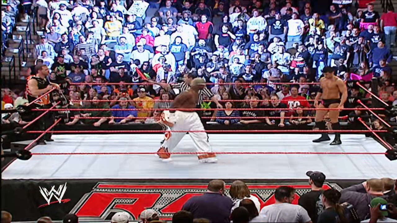 A frame from WWE Raw (October 22, 2007) at 26:19. A WWE Raw wrestling match in progress, featuring a shirtless wrestler in white pants in the center of the red-roped ring, with a referee in striped shirt nearby. The packed arena crowd fills the background, while the WWE logo and red RAW graphics are visible at the bottom of the frame.