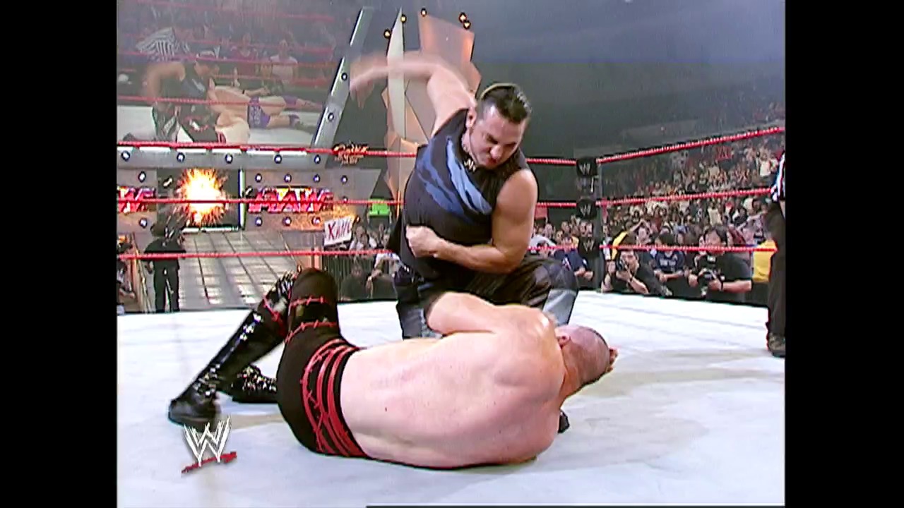 A frame from WWE Raw (May 17, 2004) at 26:44. A WWE wrestler in black attire applies a submission hold to an opponent lying on the mat in the ring, while a large crowd watches from the stands in the background. The WWE logo is visible in the lower left corner of the broadcast.