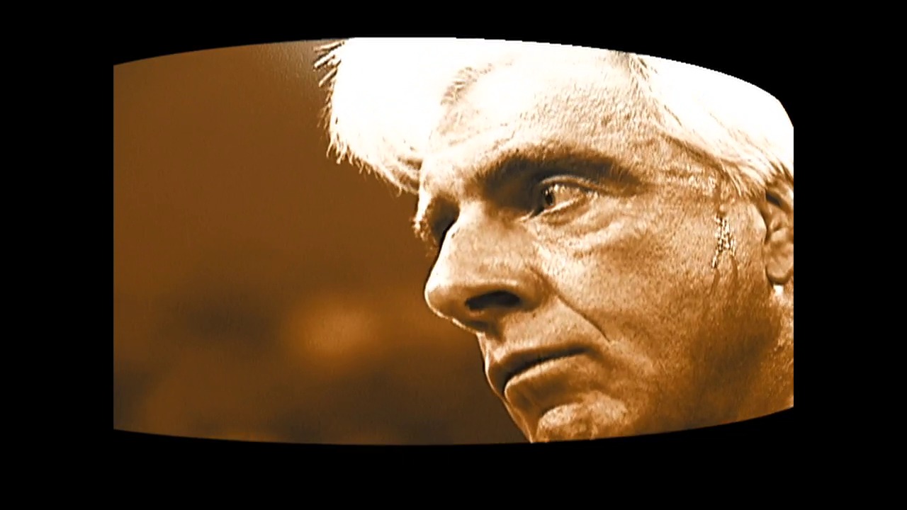 A frame from WWE Raw (January 31, 2002) at 0:30. A close-up profile view of a male wrestler's face with white/blonde hair against a brown and black background, captured during a WWE Raw broadcast from 2002.