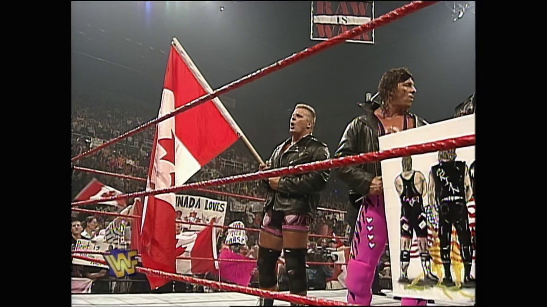 A frame from WWE Raw (July 21, 1997) at 1:26:30. # WWE Raw (July 21, 1997)

A Canadian flag is prominently displayed in a WWE wrestling ring during what appears to be a patriotic segment. Wrestlers and personnel stand in the ring while a large crowd watches from the arena, with the red ropes and WWF branding visible in the frame.