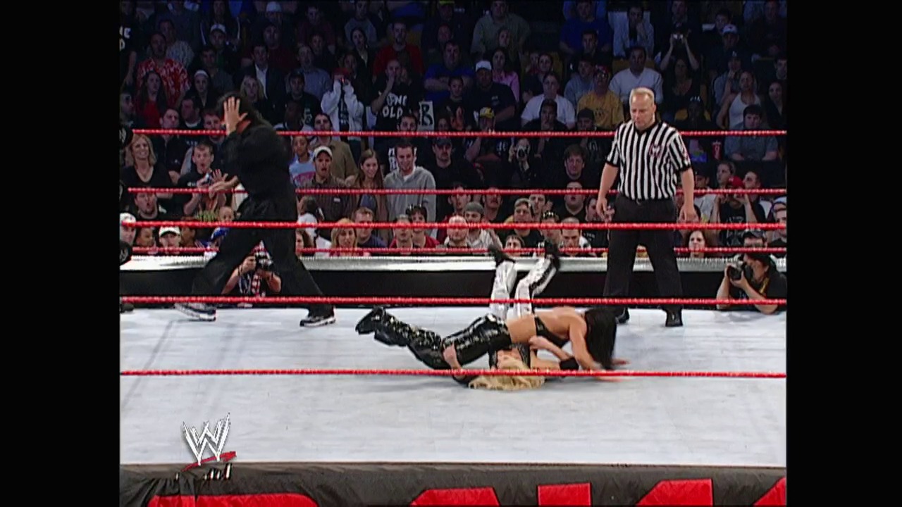 A frame from WWE Raw (April 28, 2003) at 1:21:40. A WWE wrestler lies on the mat during a match in the red-roped ring, while a referee in striped shirt observes. The crowd fills the arena seats in the background, with the WWE logo visible at the bottom of the frame.