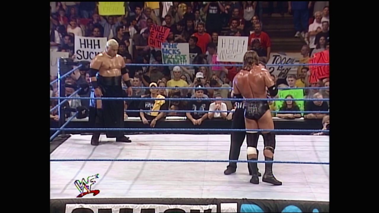 A frame from WWE SmackDown (January 6, 2000) at 1:19:32. Two shirtless wrestlers face off in a WWE ring with blue ropes, while a crowd holds signs in the background. The WWE logo is visible at the bottom of the frame.