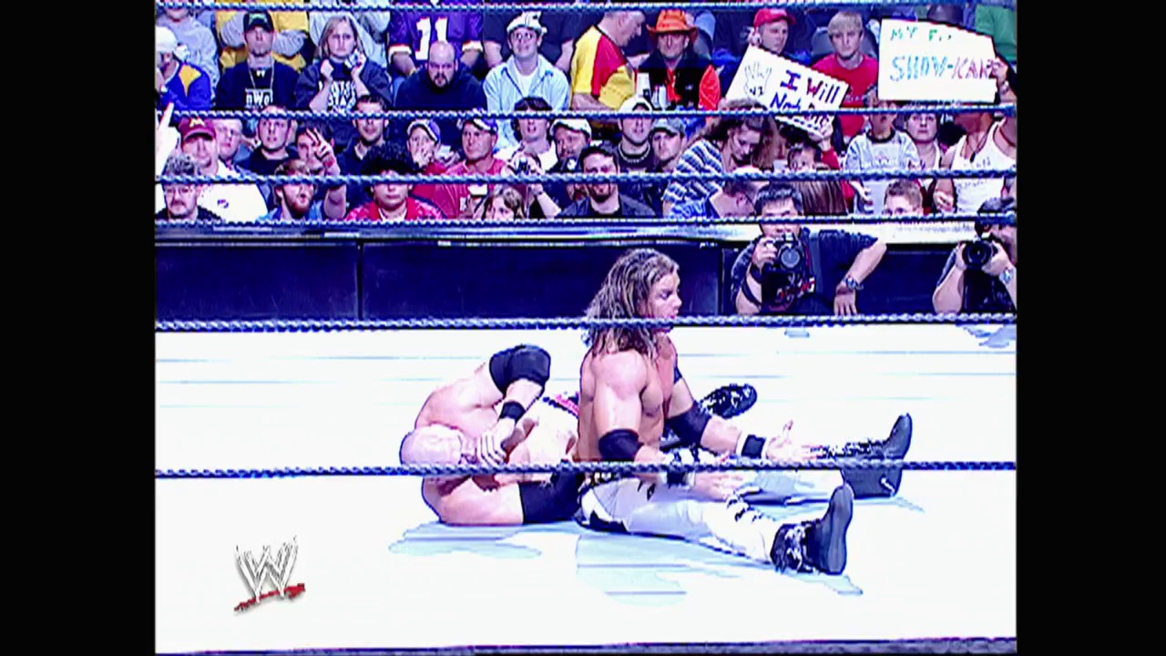 A frame from WWE Raw (November 14, 2005) at 13:34. # WWE Raw Wrestling Match

Two wrestlers grapple on the mat inside a blue-roped ring, with one applying a submission hold. The crowd fills the stands behind them, and the WWE logo appears in the lower left corner of the broadcast.