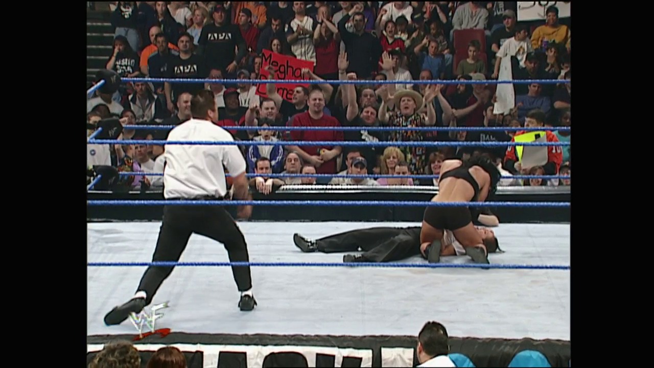 A frame from WWE SmackDown (April 12, 2001) at 37:38. A WWE wrestler in a white shirt stands in the blue-roped ring while an opponent lies on the mat below. The crowd fills the arena stands in the background, with the WWF logo visible in the lower left corner.