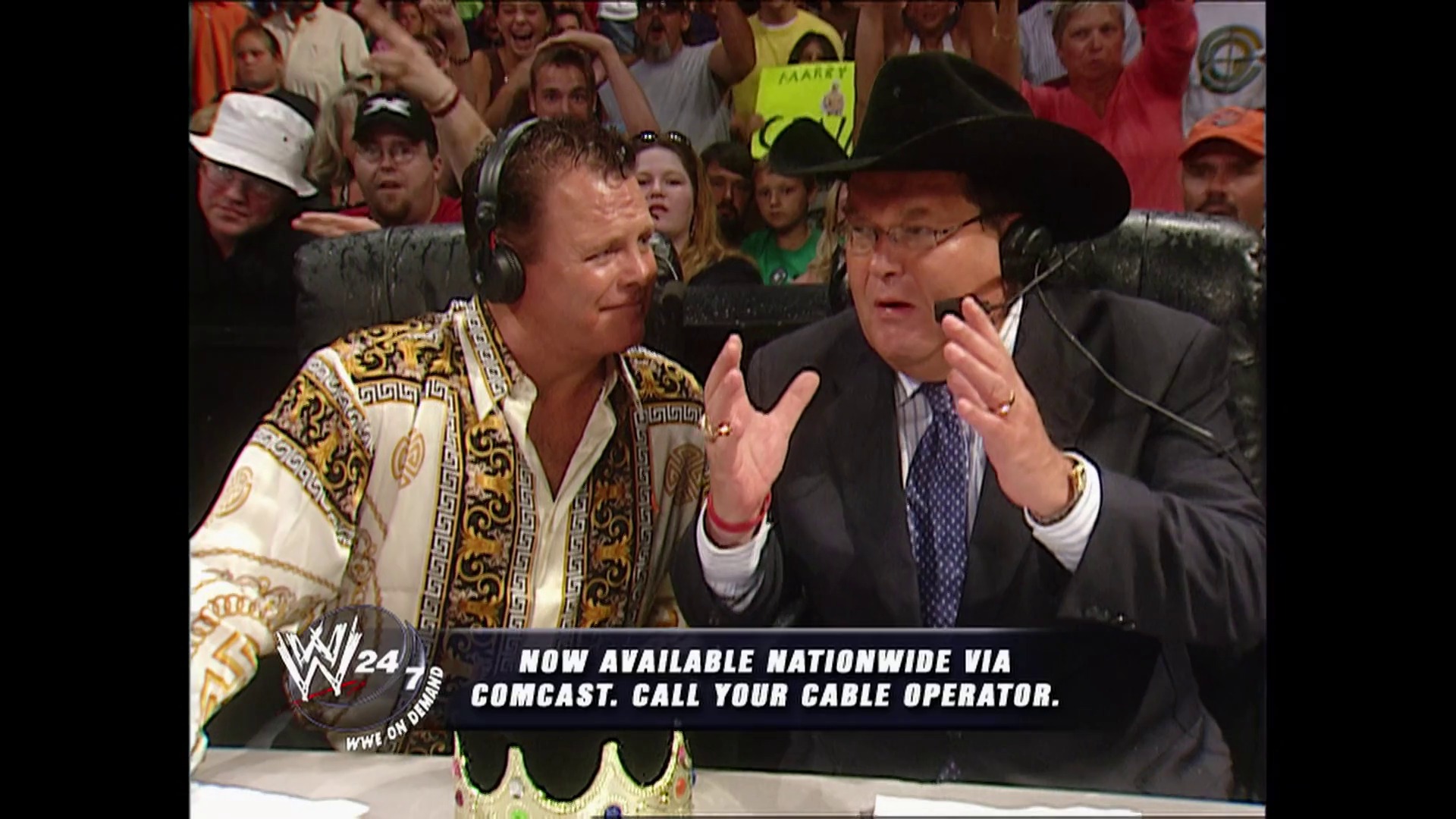 A frame from WWE Raw (August 14, 2006) at 42:00. Two commentators sit ringside wearing headsets—one in an ornate gold and cream robe, the other in a dark suit and cowboy hat. A enthusiastic crowd fills the background while a WWE graphic and Comcast advertisement appear at the bottom of the screen.