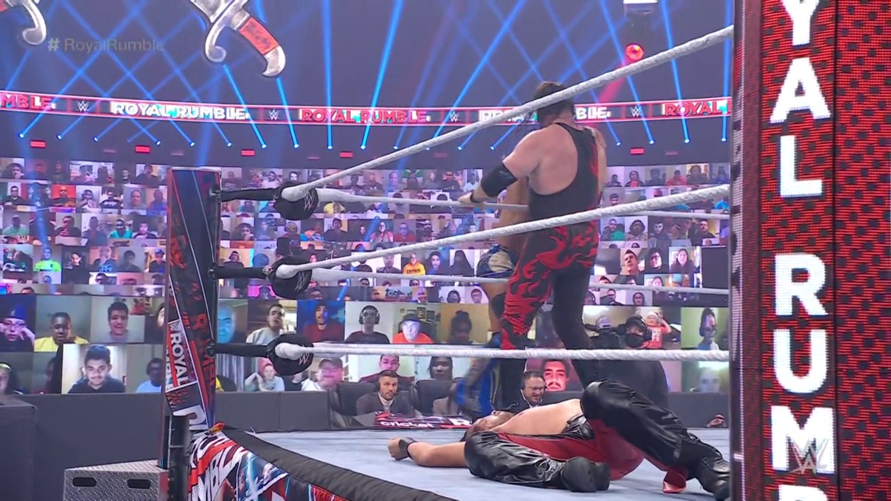 A frame from WWE: Royal Rumble (2021) at 3:15:04. A wrestler in black attire stands in the WWE ring during Royal Rumble 2021, with an opponent lying on the mat below. The arena features virtual crowd screens in the background and prominent "ROYAL RUMBLE" graphics visible on the ring barrier and signage.
