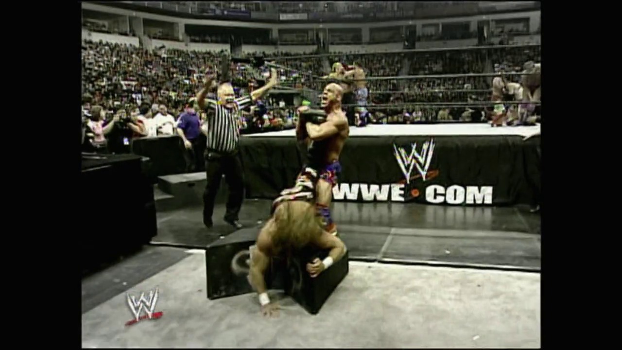 A frame from WrestleMania 21 (2005) at 1:35:55. A WWE wrestler celebrates in the ring with arms raised while another wrestler is down on the mat, as a referee stands nearby and the crowd cheers in the packed arena behind them.
