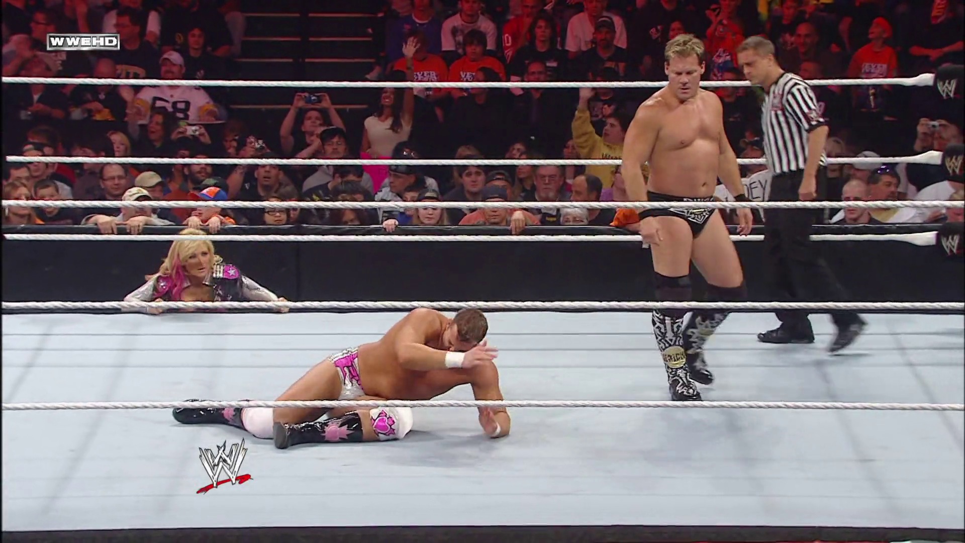 A frame from WWE Raw (May 10, 2010) at 18:00. A WWE wrestler lies on the mat in pink and black attire while an opponent stands nearby. A referee in stripes oversees the match as the crowd watches from the stands, with a female performer visible at ringside.