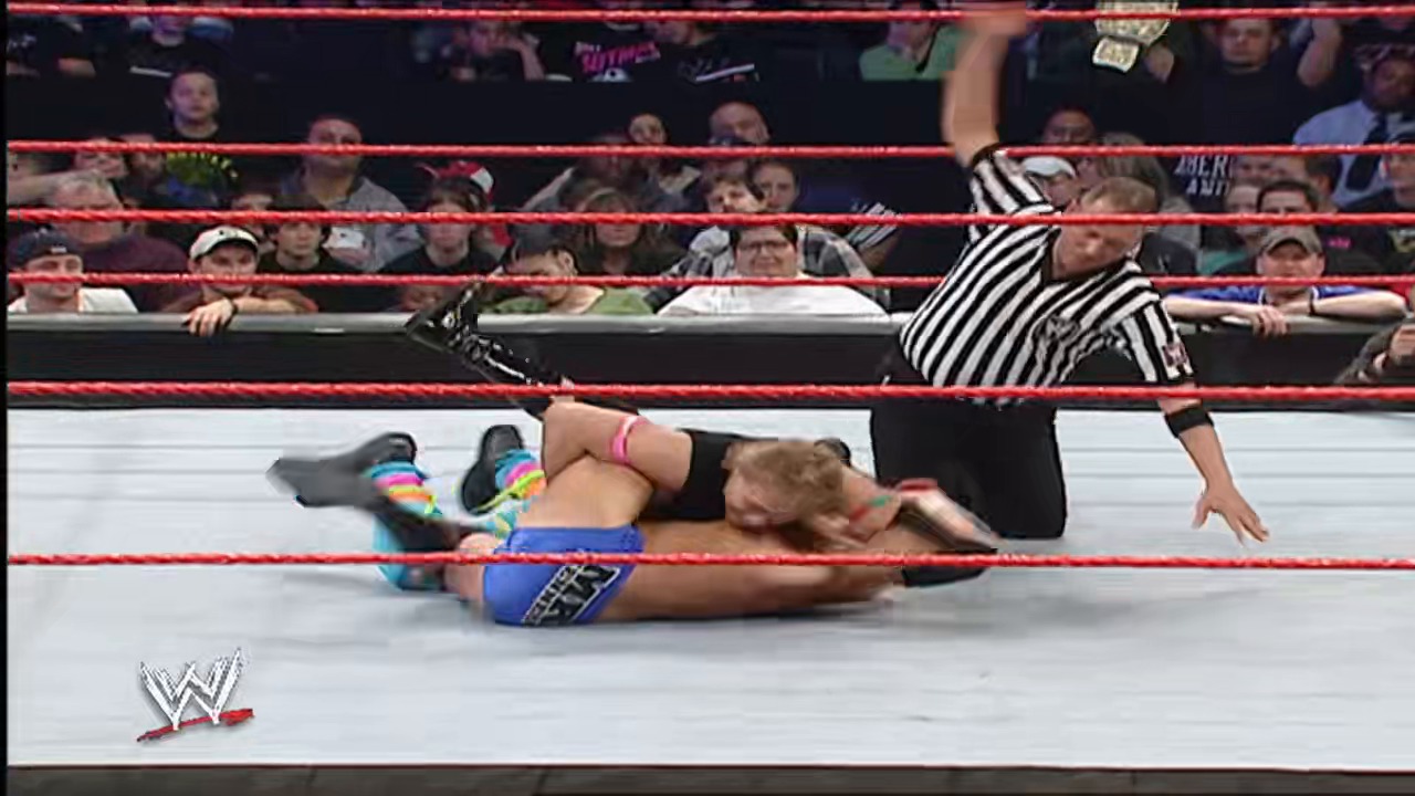 A frame from WWE Raw (December 10, 2007) at 2:01:44. A WWE wrestler lies on the mat in the red-roped ring while a referee in striped shirt stands nearby. The crowd watches from the stands as the match unfolds during this WWE Raw event.