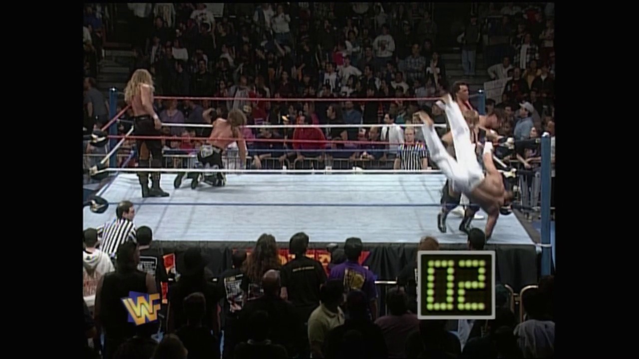 A frame from Royal Rumble (1996) at 1:37:11. A wrestler performs an aerial move in the WWF ring during Royal Rumble 1996, with the crowd and ringside personnel visible below. The match timer displays "05" in the lower right corner of the screen.