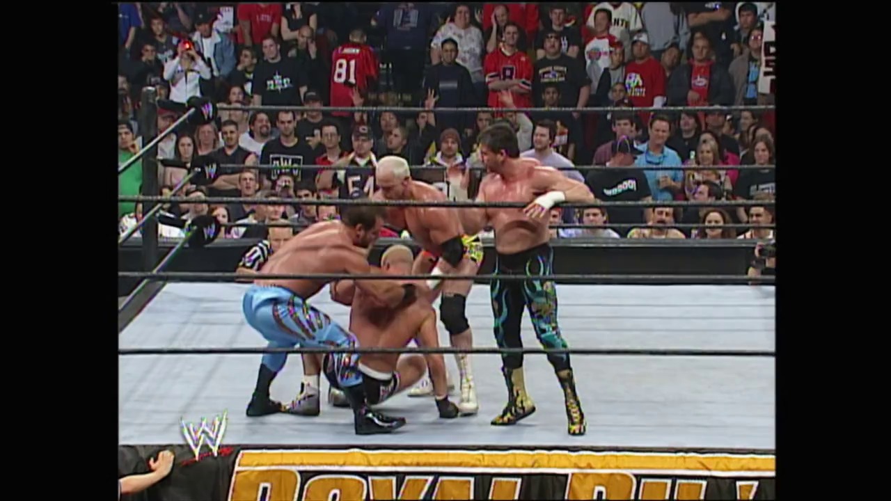 A frame from WWE Royal Rumble (2005) at 2:02:12. Multiple wrestlers engage in action inside a WWE ring surrounded by a cheering crowd. The WWE logo and event graphics are visible at the bottom of the frame, with the ring ropes and turnbuckles framing the intense in-ring competition.