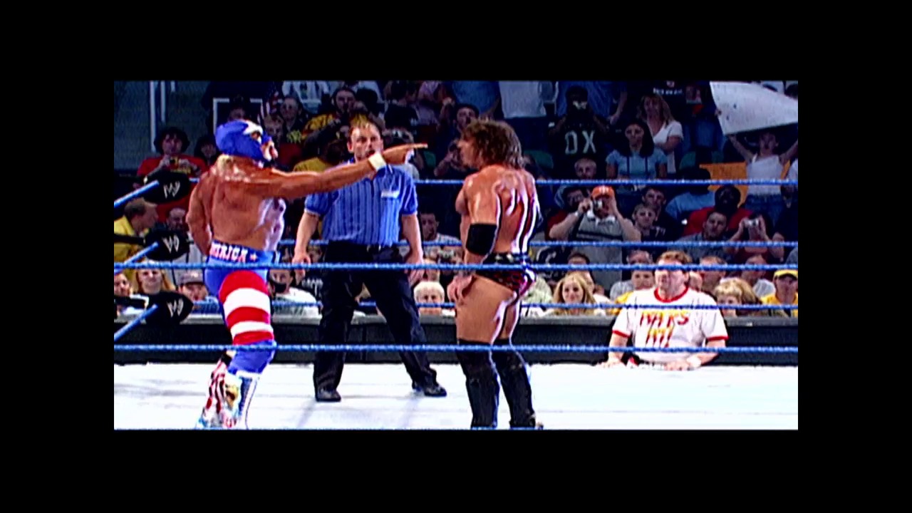 A frame from WWE SmackDown (May 29, 2003) at 0:44. A WWE wrestler in blue and red striped attire engages in action with an opponent in the ring, while a referee in a blue shirt supervises. The crowd fills the arena background, with the blue-roped wrestling ring and WWE branding visible.
