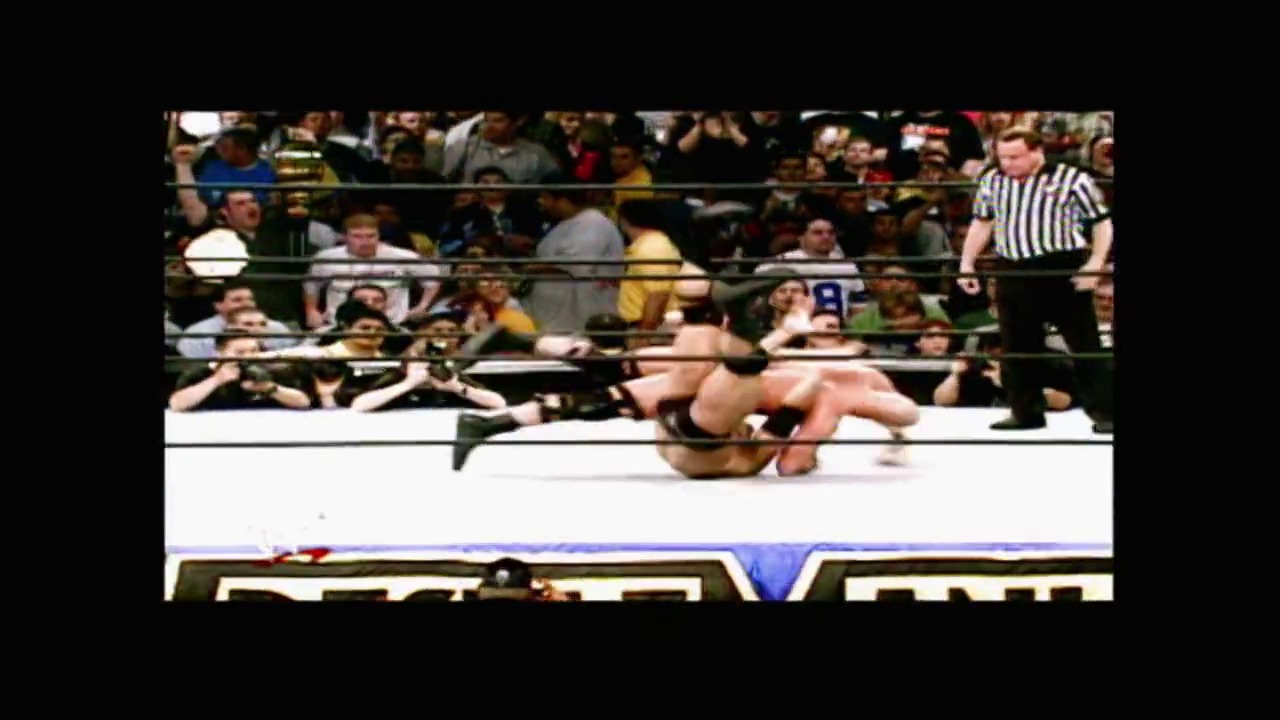 A frame from WrestleMania X-Seven (2001) at 3:44:46. # WrestleMania X-Seven Frame

A wrestler lies on the white canvas of the WWE ring during an intense match, with a referee in striped shirt nearby. The crowd fills the stands in the background, and the event's graphics are visible at the bottom of the frame.
