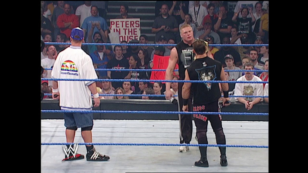 A frame from WWE SmackDown (April 17, 2003) at 25:29. A WWE SmackDown wrestling match is underway with two wrestlers in the ring—one in white attire on the left and another in black on the right. A referee stands between them as a crowd watches from the stands, with a "Peters in the House" sign visible in the background.