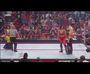 A frame from WWE Raw (February 4, 2008) at 13:14. A WWE wrestling match is underway in the ring with two wrestlers facing off while a referee stands between them. The arena is filled with enthusiastic spectators in the background, and the classic WWE ring setup is visible with its white mat and red padding.