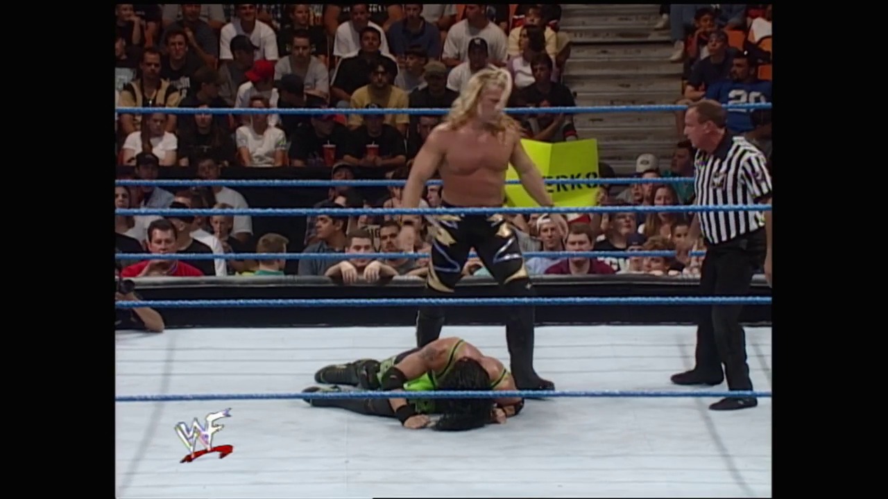 A frame from WWE SmackDown (September 2, 1999) at 38:26. A WWE SmackDown match in progress shows a shirtless blonde wrestler standing in the ring while an opponent lies on the mat. A referee in a striped shirt oversees the match as the crowd watches from the stands.