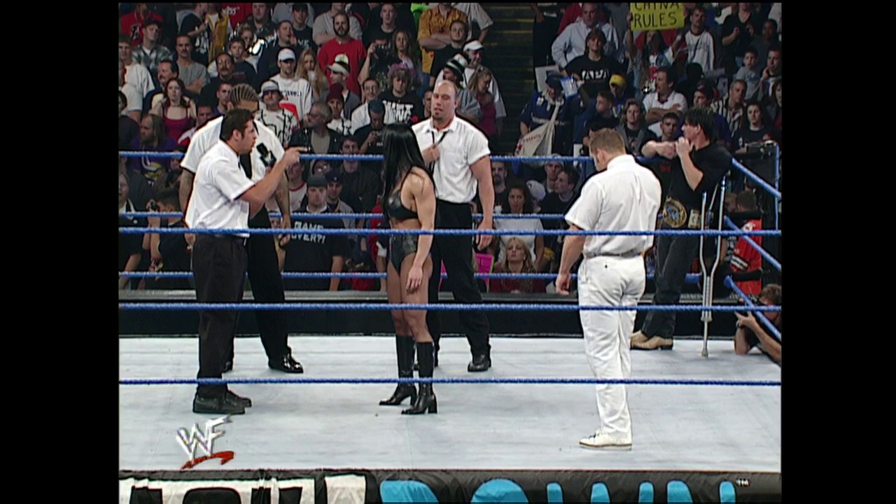 A frame from WWE SmackDown (October 19, 2000) at 26:34. A WWE wrestler stands in the center of the blue-roped ring facing two referees in white shirts and black pants, with a crowded arena visible in the background. The WWF logo appears at the bottom left of the frame.
