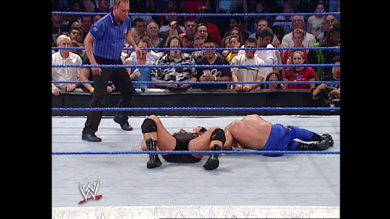 A frame from WWE SmackDown (June 19, 2003) at 24:33. A wrestler lies on the mat in a WWE SmackDown ring while a referee stands nearby and the crowd watches from the stands. The WWE logo is visible in the lower left corner of the broadcast.
