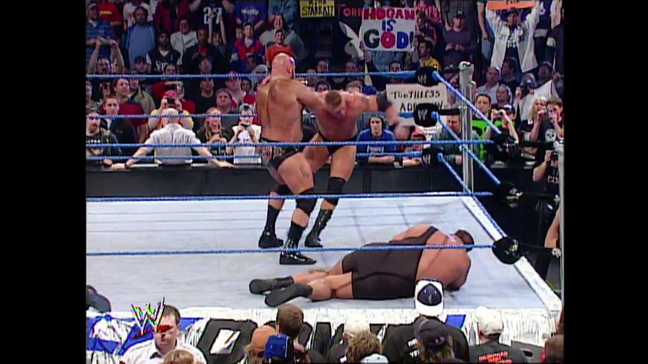A frame from WWE SmackDown (May 8, 2003) at 1:25:04. A WWE SmackDown match in progress shows two wrestlers in the ring—one standing in an aggressive pose while another lies on the mat. The crowd fills the arena behind the blue-roped ring, with commentators visible at ringside.