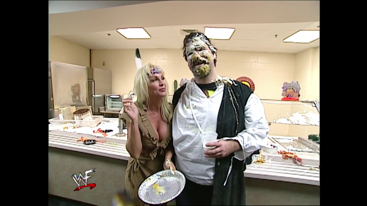A frame from WWE SmackDown (November 23, 2000) at 1:13:50. Two wrestlers in costume stand in what appears to be a backstage kitchen set, with one wearing an elaborate beast-like mask and the other in casual attire. A WWF logo is visible in the lower left corner of the screen.