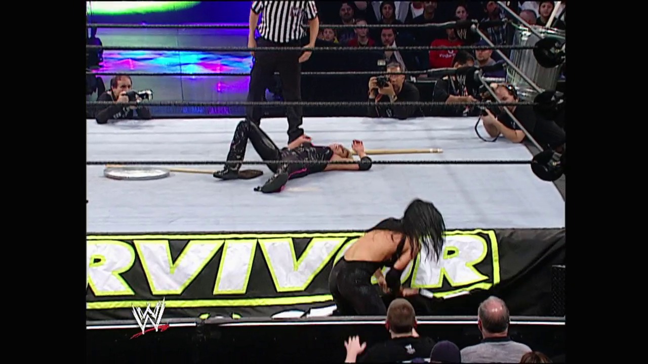 A frame from Survivor Series (2002) at 47:17. A WWE wrestler lies prone on the ring mat during Survivor Series 2002, while another performer stands nearby. The crowd watches from the arena as officials and cameramen document the match, with the event's logo visible on the ring apron.
