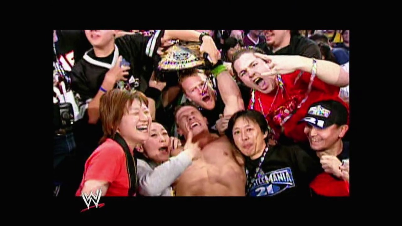 A frame from WrestleMania 21 (2005) at 3:44:20. A shirtless wrestler celebrates surrounded by excited fans and crew members at WrestleMania 21. The WWE logo is visible in the corner, capturing the energetic atmosphere of the live event.